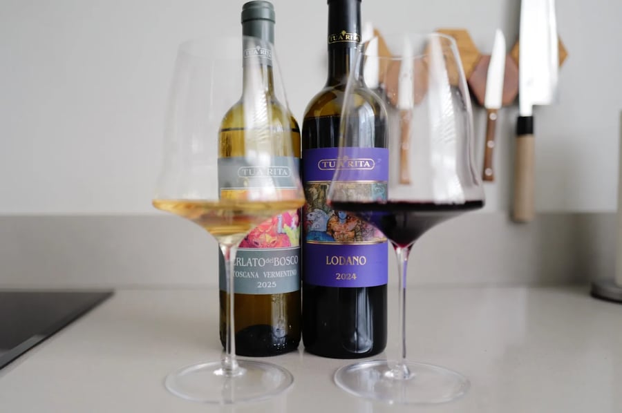 Fles Perlato del Bosco Vermentino 2025 en fles Lodano 2024 van Tua Rita naast elkaar op het aanrecht, met een glas witte en een glas rode wijn