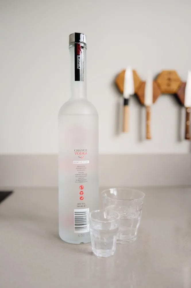 Achterkant van de Chance Vodka-fles met productie-informatie uit Polen, naast twee glazen