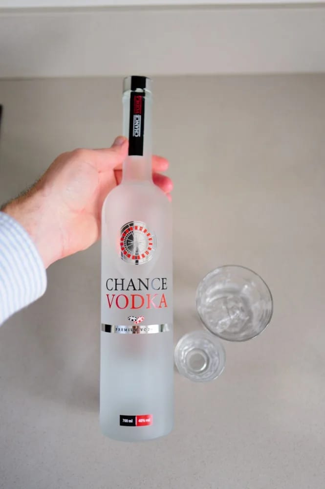 Hand houdt de gevroren fles Chance Vodka vast boven het aanrecht, met twee glazen ernaast