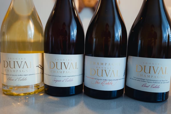 Vier flessen Champagne Edouard Duval naast elkaar op een houten tafel, met het wijngaardlandschap van Côte des Bar op de achtergrond.